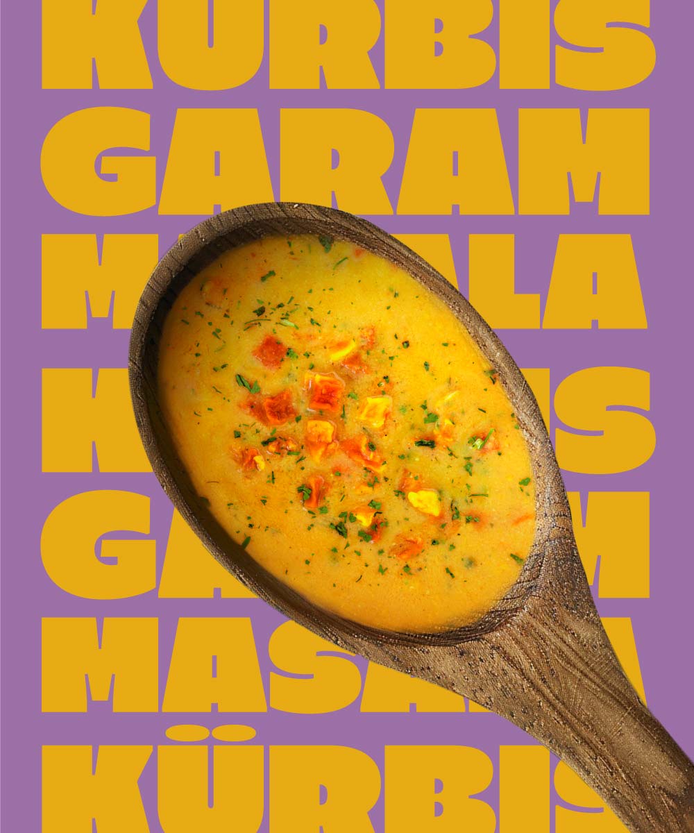 Ein Holzlöffel in dem Miss Mineva's fermentierte Suppe mit Geschmacksrichtung Kürbis-Garam-Masala vor einem bunten Hintergrund zu sehen ist