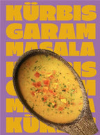 Ein Holzlöffel in dem Miss Mineva's fermentierte Suppe mit Geschmacksrichtung Kürbis-Garam-Masala vor einem bunten Hintergrund zu sehen ist